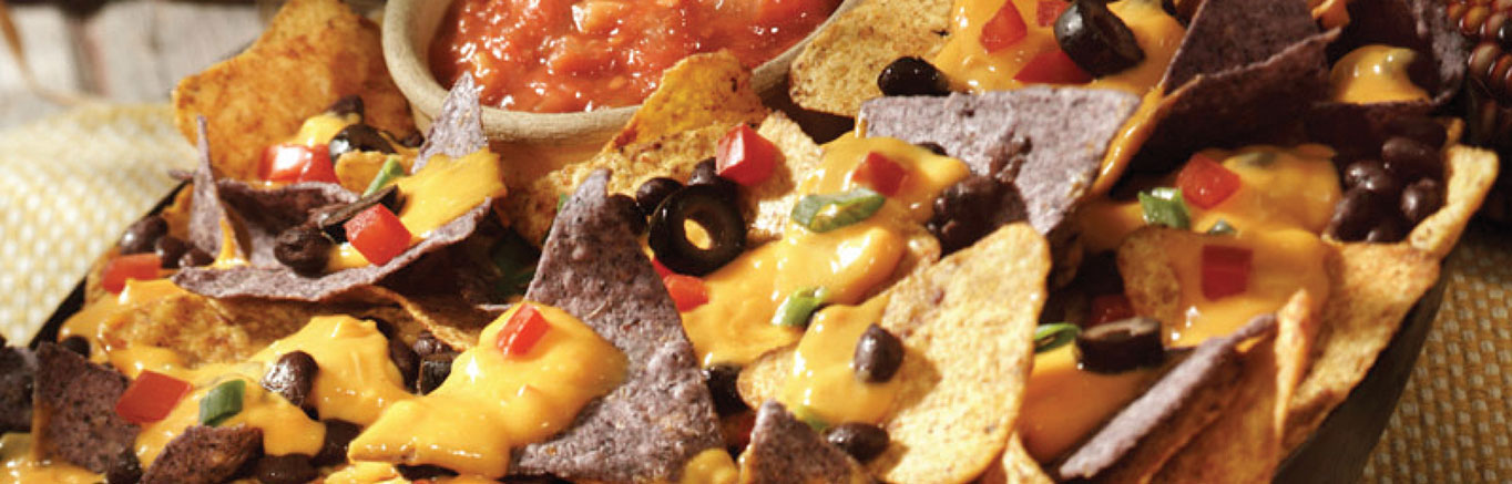 An image of prepared Deluxe Nachos made with Pace® Salsa con Queso, tortilla chips, black beans, tomato, black olives and green onion.