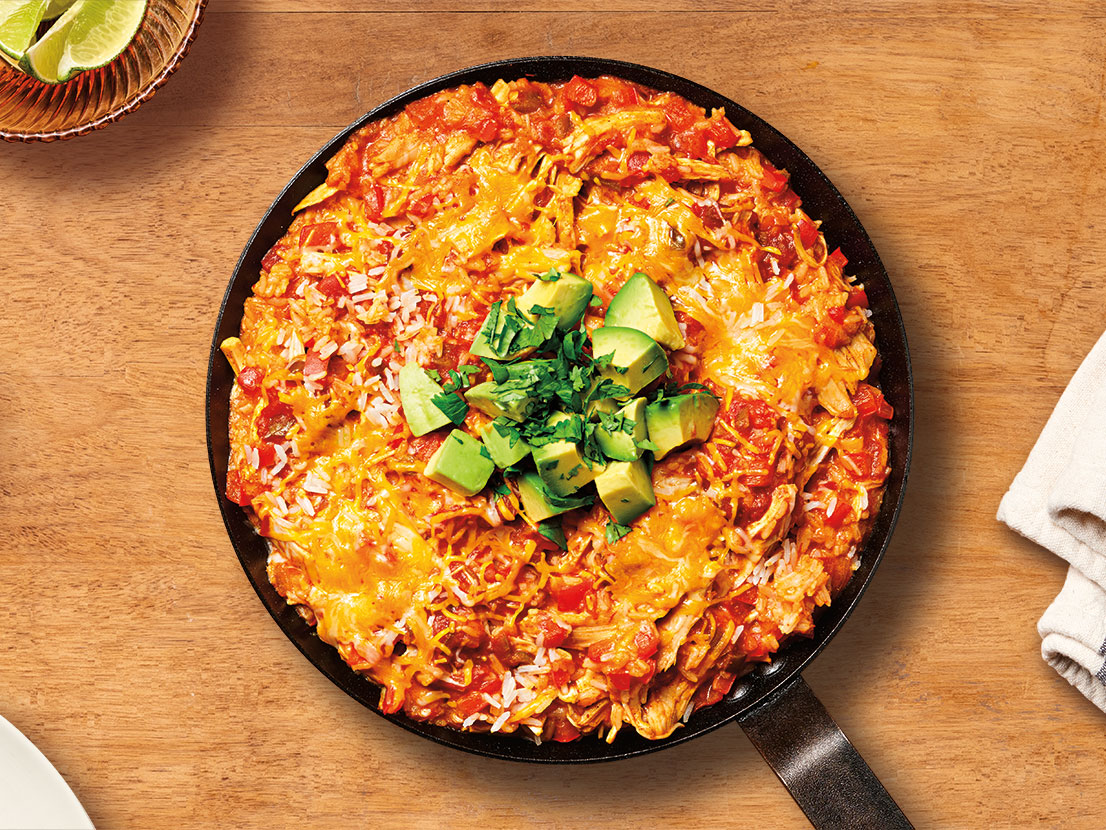 An image of prepared Easy Chicken Enchilada Skillet showing red bell pepper, garlic, Campbell's® Condensed Cream of Chicken Soup, Pace® Chunky Salsa, cooked chicken or thighs, instant white rice, Mexican blend cheese, cilantro, avocado and lime.