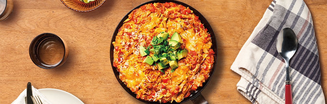 An image of prepared Easy Chicken Enchilada Skillet showing red bell pepper, garlic, Campbell's® Condensed Cream of Chicken Soup, Pace® Chunky Salsa, cooked chicken or thighs, instant white rice, Mexican blend cheese, cilantro, avocado and lime.