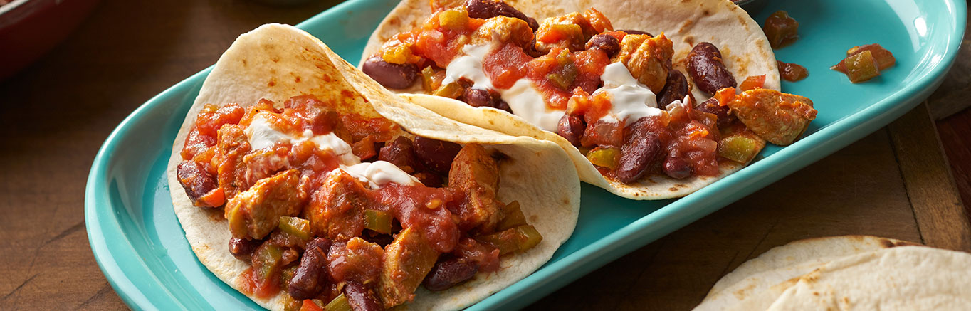 An image of prepared Cajun Chicken Tacos made with chicken, Cajun seasoning, Pace® Chunky Salsa, bell pepper, kidney beans, sour cream and tortillas.