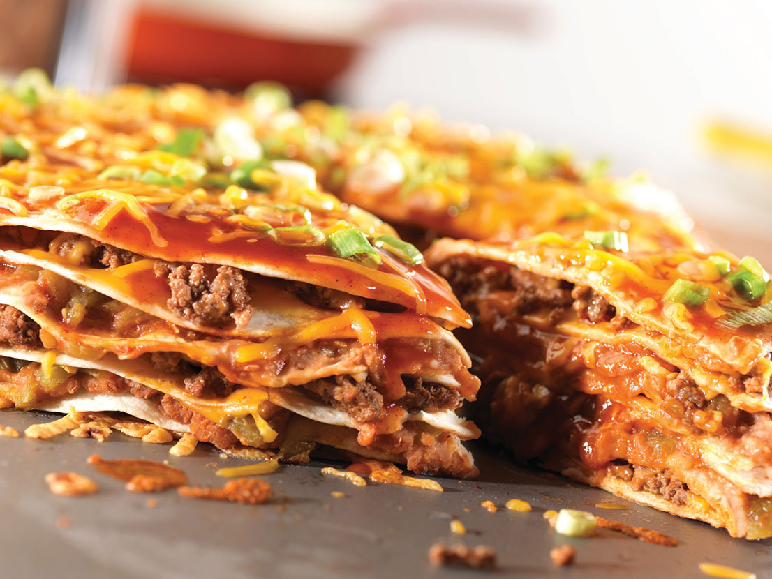 An image of prepared Cheesy Enchilada Stack made with ground beef, enchilada sauce, flour tortillas, Cheddar cheese, refried beans, green chiles, green onions and Pace® Chunky Salsa.