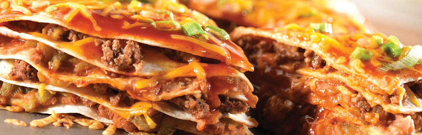 An image of prepared Cheesy Enchilada Stack made with ground beef, enchilada sauce, flour tortillas, Cheddar cheese, refried beans, green chiles, green onions and Pace® Chunky Salsa.
