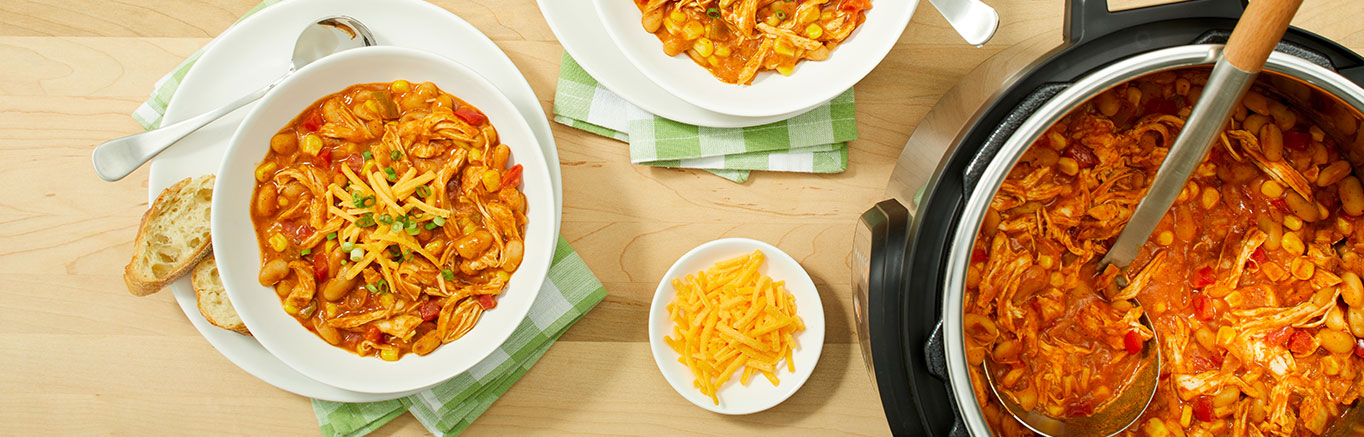 An image of prepared Instant Pot® White Chicken Chili made with red bell pepper, corn, chicken, white cannellini beans, Pace® Chunky Salsa, Campbell's® Condensed Cream of Chicken Soup, Cheddar cheese and green onion.
