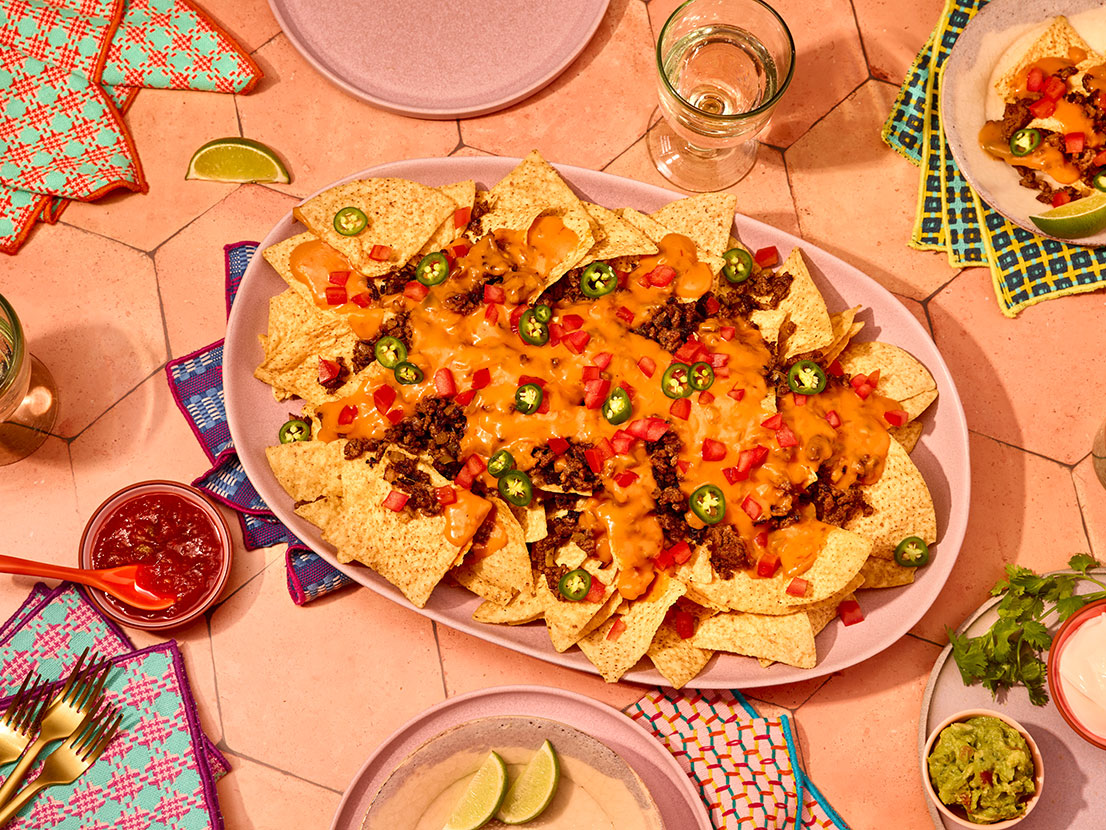 An image of prepared Nachos Grande made with Pace® Mild Nacho Cheese Sauce, Pace® Picante Sauce, ground beef, onion, tortilla chips, tomato, green onion and cilantro.