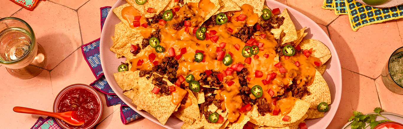 An image of prepared Nachos Grande made with Pace® Mild Nacho Cheese Sauce, Pace® Picante Sauce, ground beef, onion, tortilla chips, tomato, green onion and cilantro.