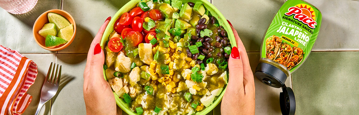 An image of prepared Cilantro Jalapeño Lime Protein Bowls made with Swanson® Natural Goodness® Chicken Broth, white rice, corn, black beans, Pace® Signature Sauces Cilantro Jalapeño Lime Sauce, chicken, tomatoes, avocado, queso fresco, green onion and cilantro.