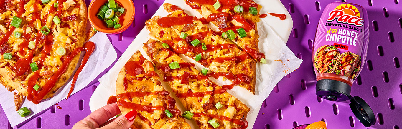 An image of prepared Hot Honey Chipotle Chicken & Bacon Flatbreads made with naan, Pace® Signature Sauces Hot Honey Chipotle Sauce, rotisserie chicken, Cheddar cheese, bacon, green onion and blue cheese.