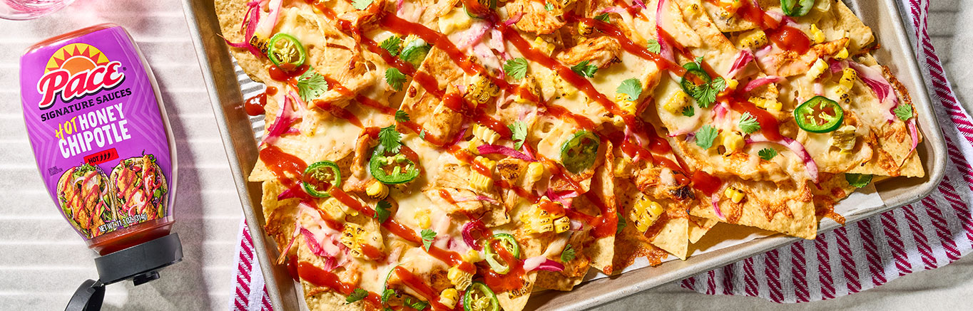 An image of prepared Hot Honey Chipotle Chicken Nachos made with chicken, Pace® Signature Sauces Hot Honey Chipotle Sauce, tortilla chips, corn, jalapeño, white Cheddar cheese, red onion and cilantro.