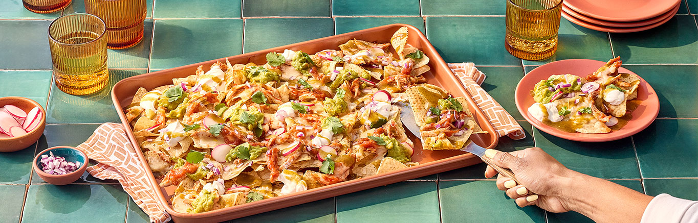 An image of prepared Chicken Tinga Nachos made with Pace® Chunky Salsa, Pace® Signature Sauces Hot Honey Chipotle Sauce, chicken, tortilla chips, Monterey Jack cheese, sour cream, guacamole, Pace® Signature Sauces Cilantro Jalapeño Lime Sauce, radishes and cilantro.