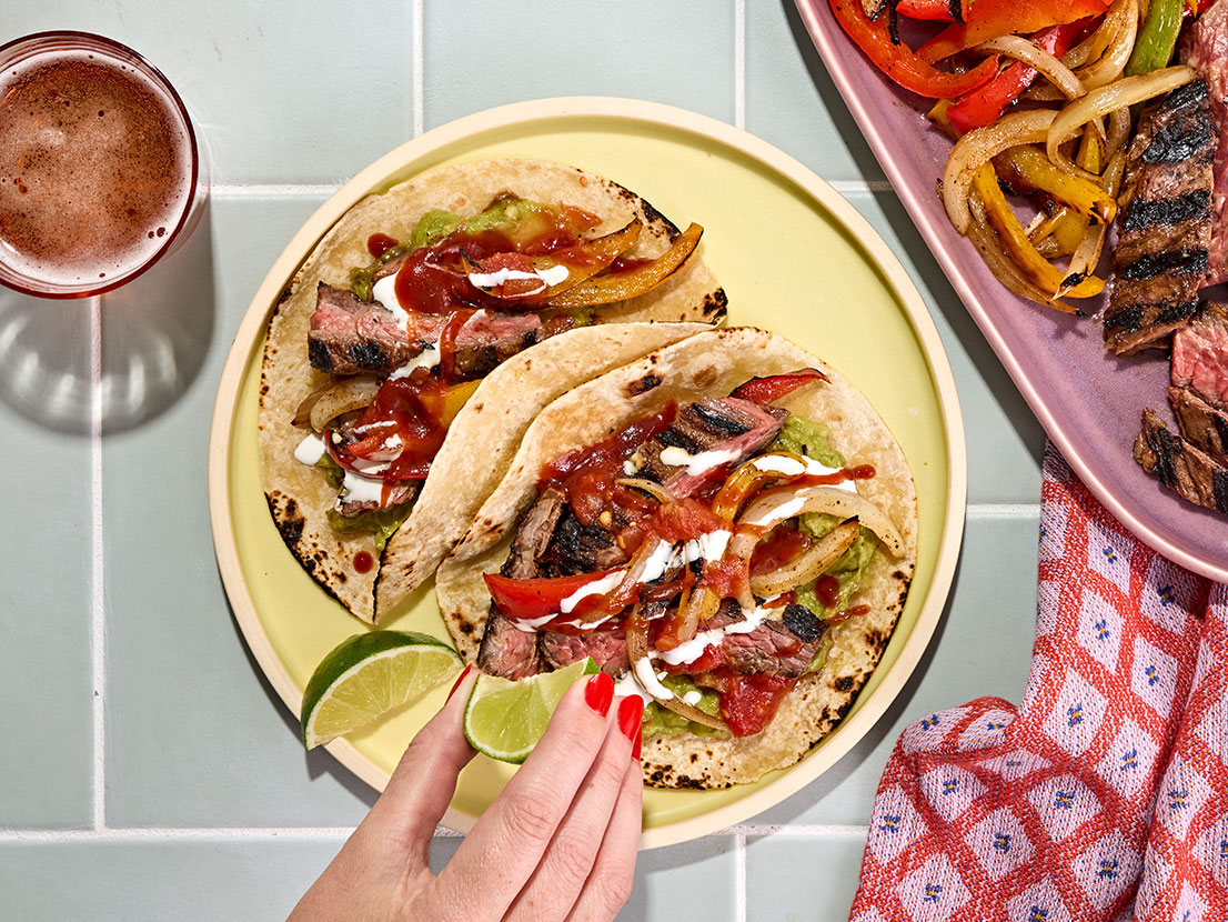 An image of prepared Hot Honey Chipotle Skirt Steak Fajitas made with Pace® Signature Sauces Hot Honey Chipotle Sauce, skirt steak, bell peppers, white onion, flour tortillas, Pace® Chunky Salsa, guacamole and crema Mexicana.