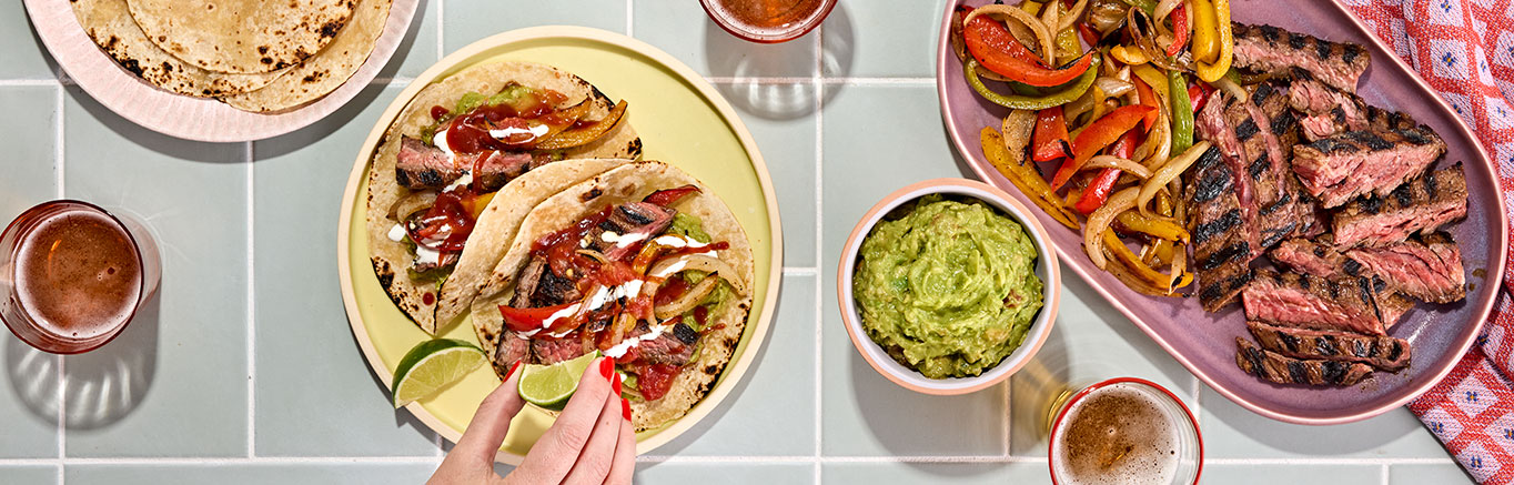 An image of prepared Hot Honey Chipotle Skirt Steak Fajitas made with Pace® Signature Sauces Hot Honey Chipotle Sauce, skirt steak, bell peppers, white onion, flour tortillas, Pace® Chunky Salsa, guacamole and crema Mexicana.