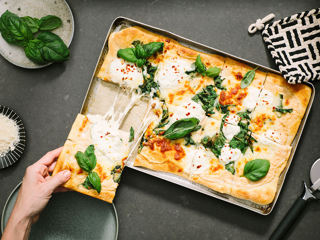 An image of prepared Sheet Pan Spinach and Cheese White Pizza made with Prego® Homestyle Alfredo Sauce, refrigerated pizza crust, baby spinach, mozzarella, Parmesan and ricotta cheese.