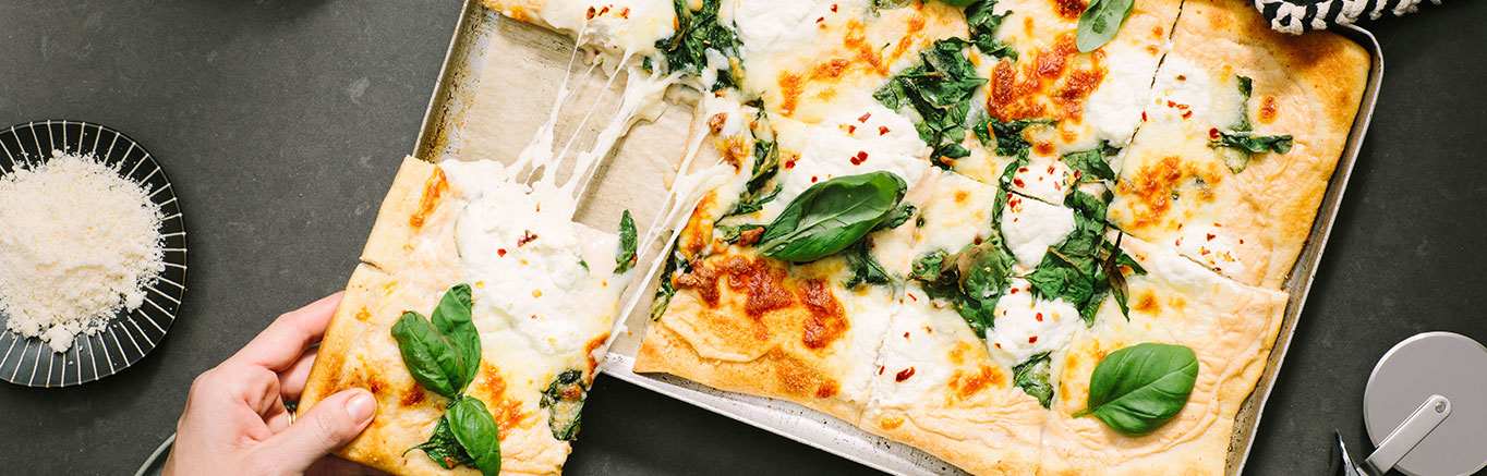 An image of prepared Sheet Pan Spinach and Cheese White Pizza made with Prego® Homestyle Alfredo Sauce, refrigerated pizza crust, baby spinach, mozzarella, Parmesan and ricotta cheese.