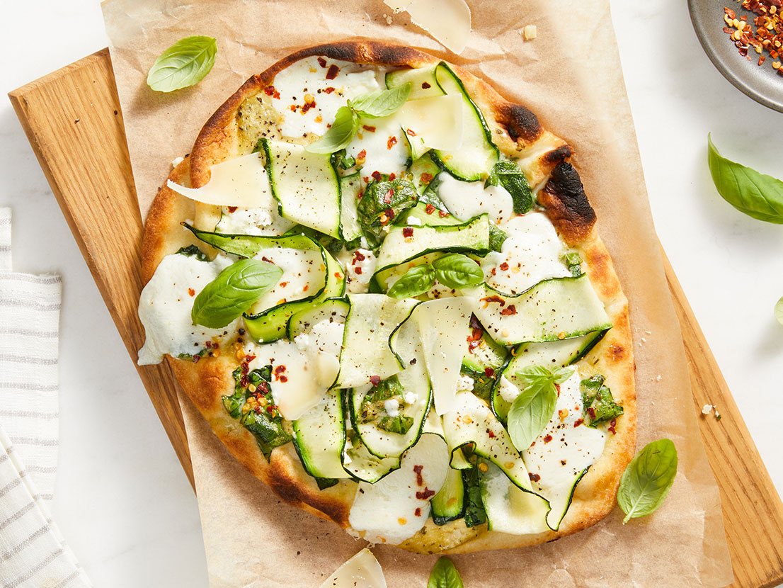 An image of prepared Creamy Pesto Flatbreads made with Prego® Creamy Roasted Garlic Pesto Sauce, spinach, naan, mozzarella, feta, zucchini and Parmesan.
