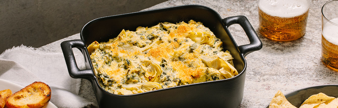 An image of prepared Pesto Spinach and Artichoke Dip made with artichoke hearts, garlic, Prego® Creamy Parmesan Pesto Sauce, cream cheese and spinach.