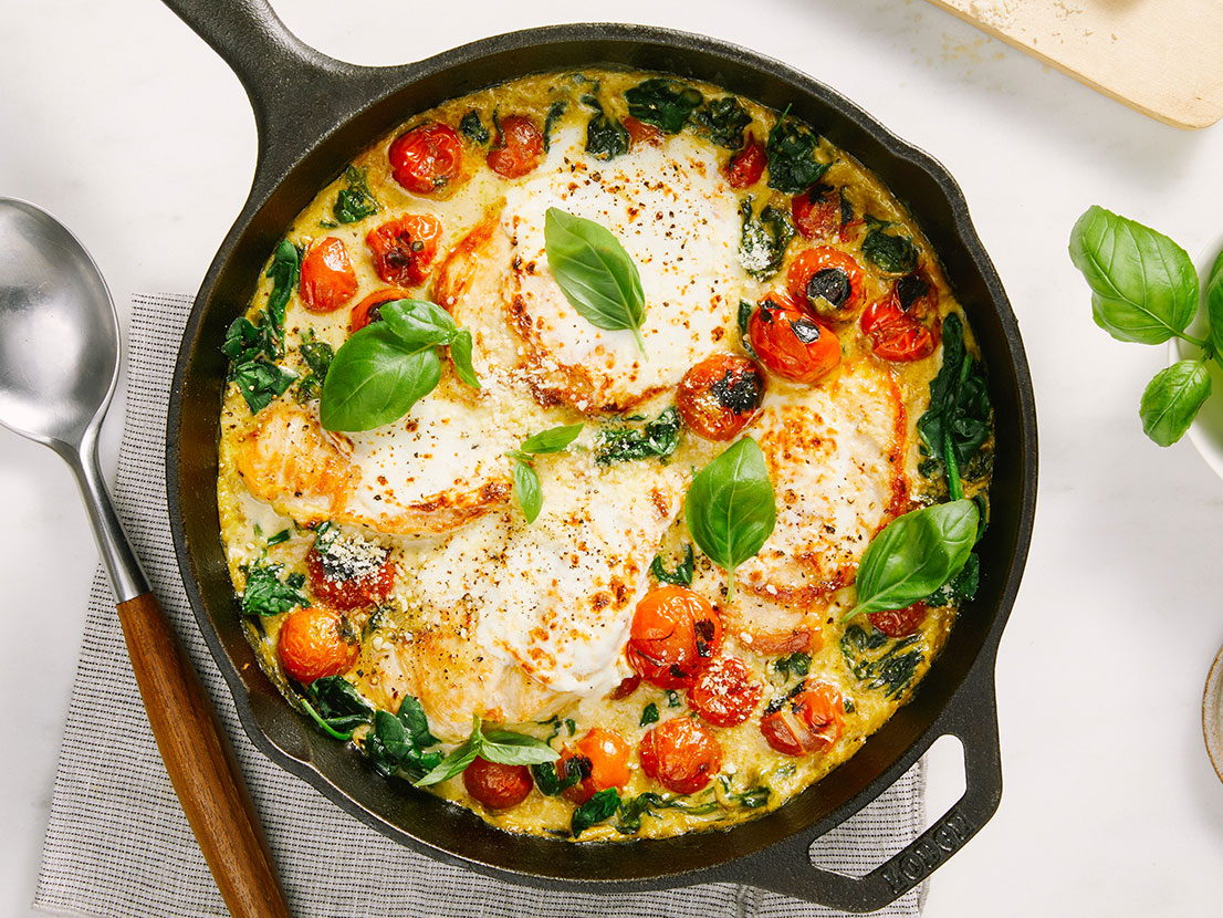 An image of prepared Skillet Creamy Pesto Chicken Caprese made with chicken, tomatoes, Prego® Creamy Parmesan Pesto Sauce, spinach, mozzarella and Parmesan cheese.