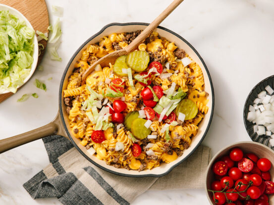An image of prepared Bacon Cheeseburger Pasta Skillet made with Prego® Creamy Cheddar Sauce, ground beef, rotini, onion, dill pickles, cherry tomatoes and lettuce.