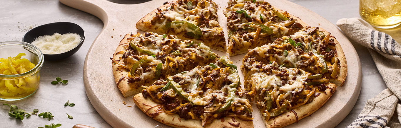 An image of prepared Cheesesteak Pizza made with Prego® Creamy Cheddar Sauce, ground beef, onion, bell pepper, mushrooms and Italian cheese blend.