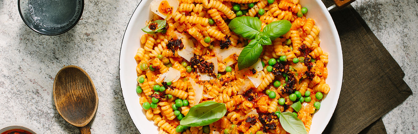 An image of prepared Chili Crisp Pasta alla Vodka made with Prego® Spicy Vodka Sauce, rotini or fusilili corti bucati, onion, chili crisp, peas and Parmesan cheese.