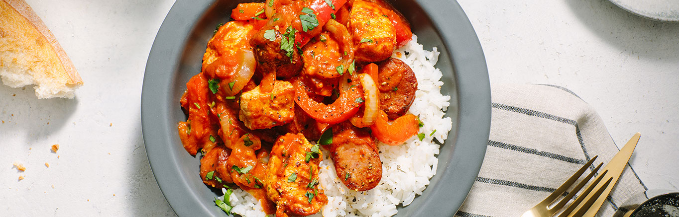 An image of prepared Creamy Tomato Cajun Chicken and Andouille Sausage made with Prego® Creamy Tomato with Garlic Sauce, white rice, chicken, Cajun seasoning, andouille sausage, onion, bell pepper and parsley.