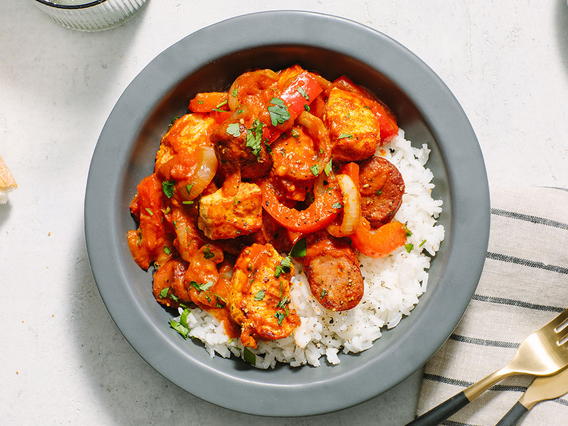 An image of prepared Creamy Tomato Cajun Chicken and Andouille Sausage made with Prego® Creamy Tomato with Garlic Sauce, white rice, chicken, Cajun seasoning, andouille sausage, onion, bell pepper and parsley.