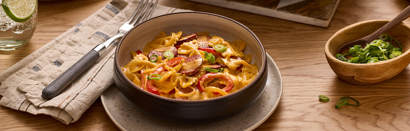 An image of prepared One Pot Smoky Cheddar Kielbasa Pasta made with Prego® Cheesy Bacon Cheddar Cheese Sauce, turkey kielbasa, onion, bell pepper, farfalle and green onion.