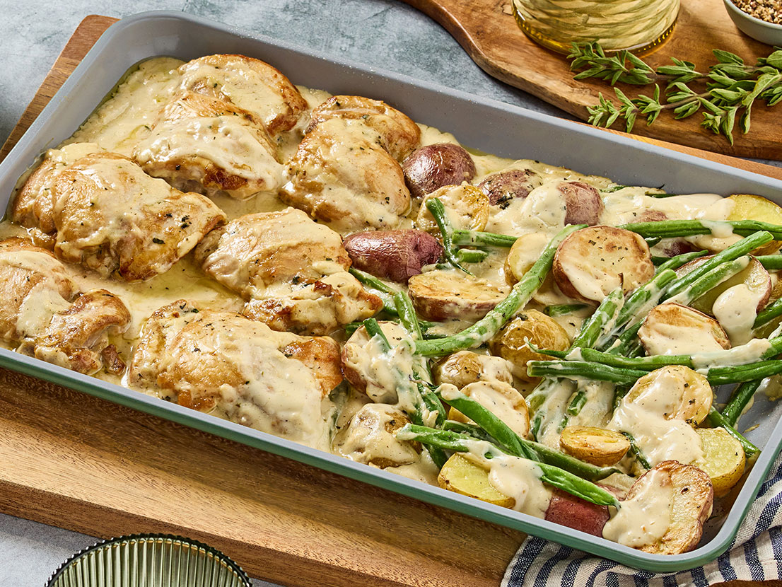 An image of prepared Creamy Lemon Sheet Pan Chicken & Potatoes made with chicken thighs. baby potatoes, oregano, green beans and Prego® Lemon Alfredo Sauce.
