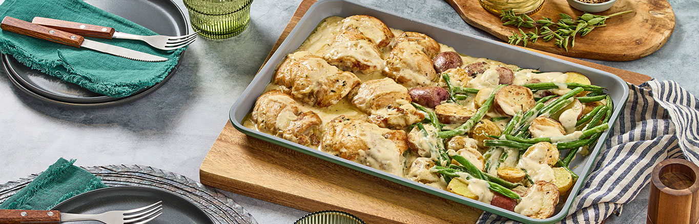 An image of prepared Creamy Lemon Sheet Pan Chicken & Potatoes made with chicken thighs. baby potatoes, oregano, green beans and Prego® Lemon Alfredo Sauce.