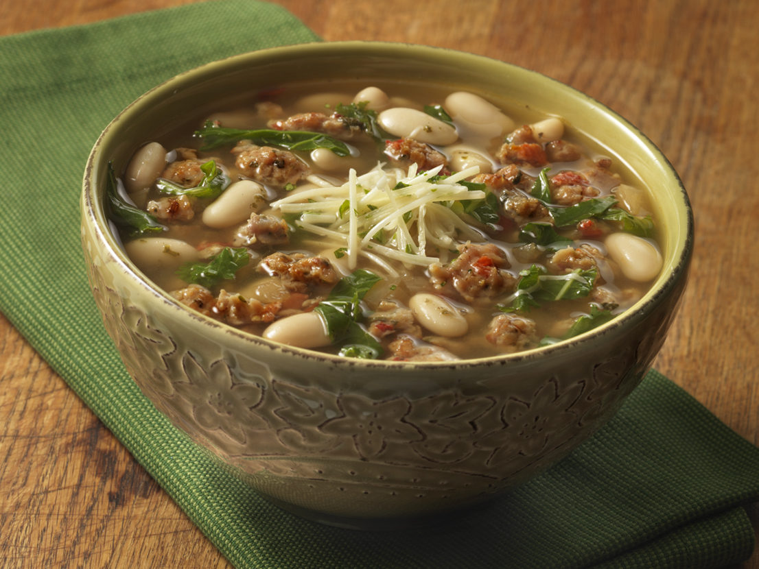 An image of prepared Tuscan White Bean Soup made with Italian-style chicken sausage, onion, white wine, Swanson® Natural Goodness® Chicken Broth, kale, cannellini beans, parsley and Parmesan cheese.