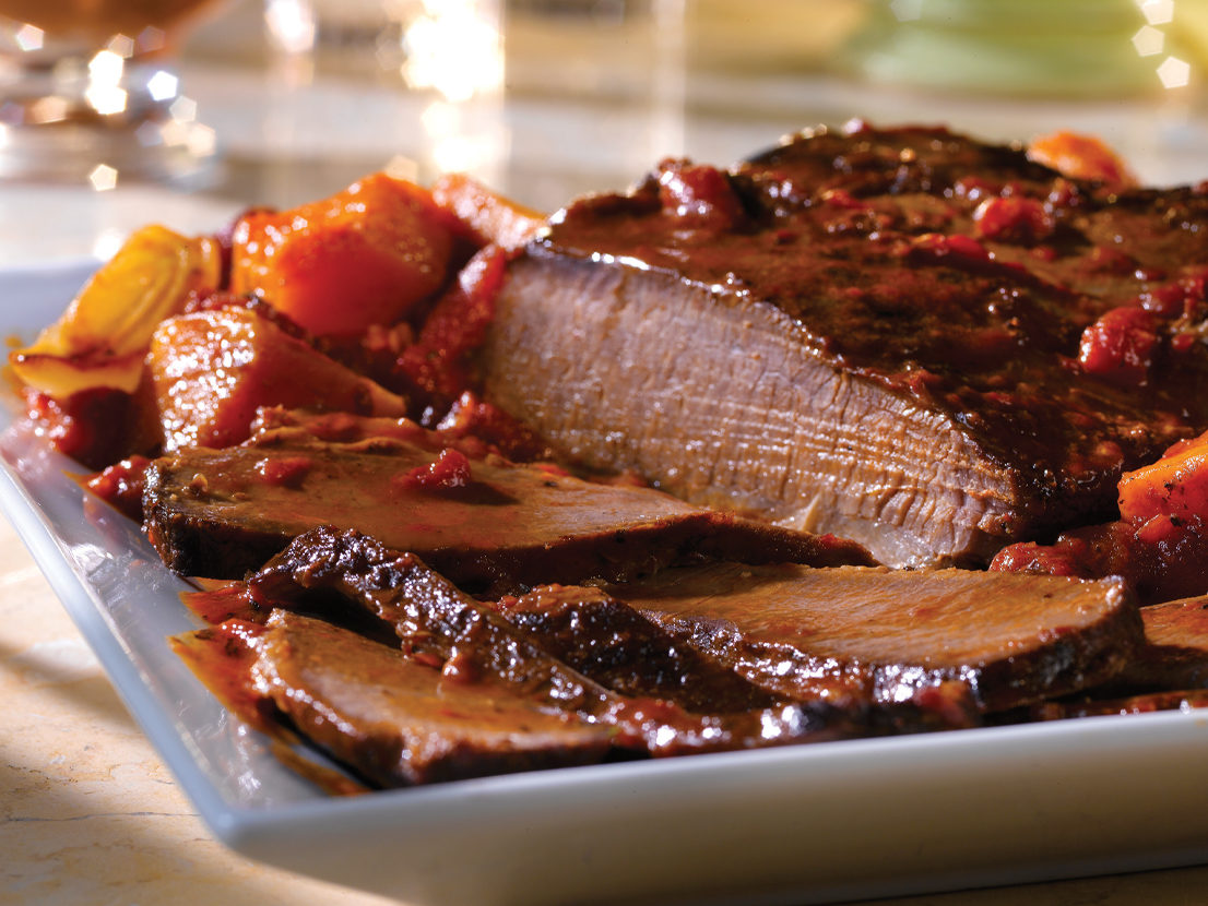 An image of prepared Holiday Brisket with Savory Onion Jus made with onion, butternut squash, beef brisket, Swanson® Beef Broth, orange juice, red wine, brown sugar and tomatoes.