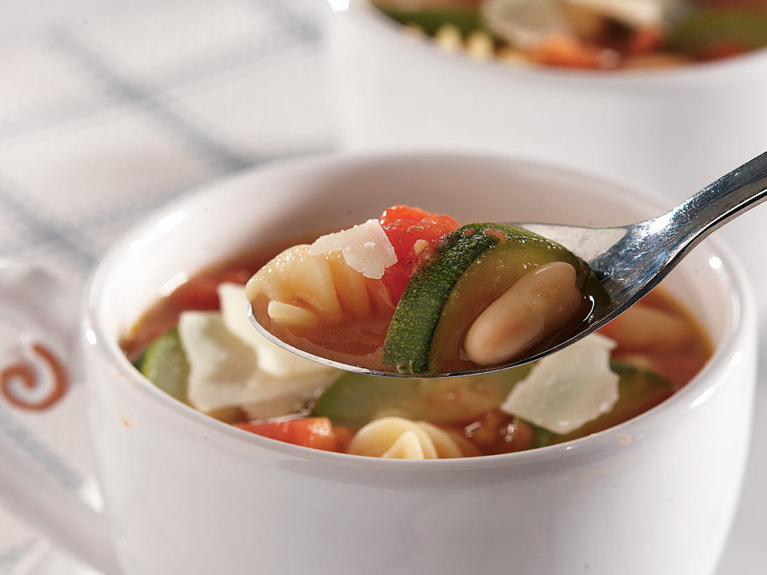 An image of prepared Vegetable Minestrone Soup made with carrot, green beans, zucchini, Swanson® Vegetable Broth, canned diced tomatoes, white cannellini beans, rotini pasta and Parmesan.