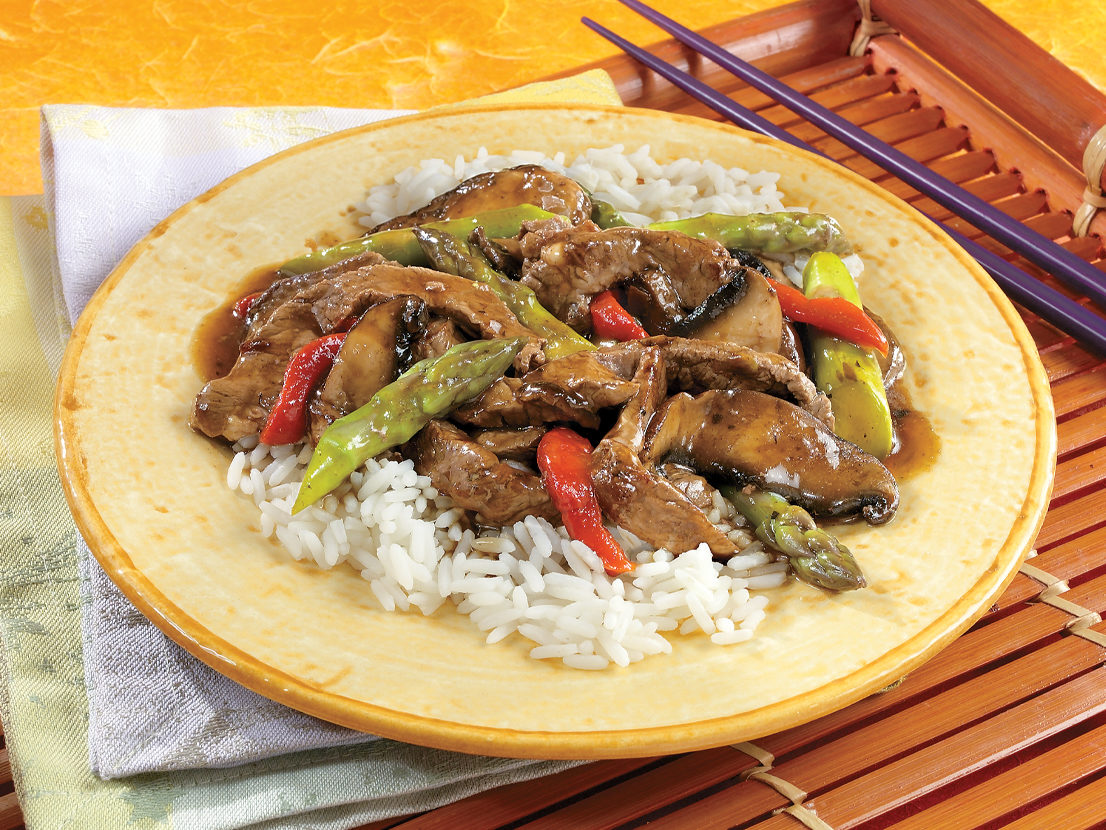 An image of prepared Asparagus & Portobello Stir-Fry made with Swanson® Beef Broth, beef sirloin steak, asparagus, portobello mushrooms, red bell peppers and long grain white rice.