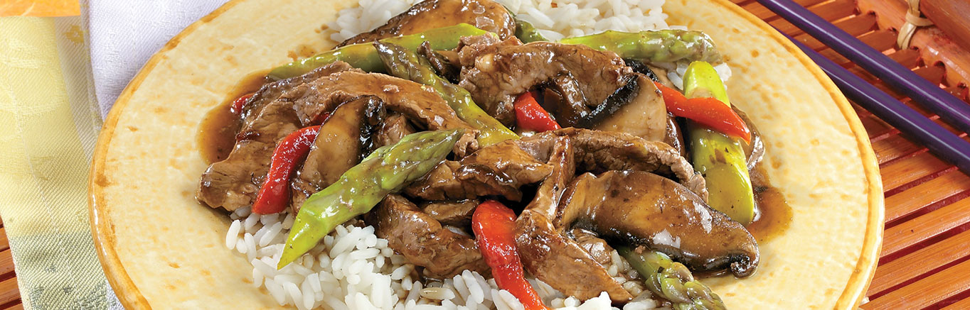 An image of prepared Asparagus & Portobello Stir-Fry made with Swanson® Beef Broth, beef sirloin steak, asparagus, portobello mushrooms, red bell peppers and long grain white rice.