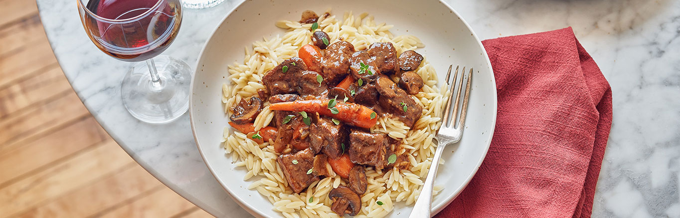 An image of prepared Beef Bourguignon made with beef sirloin steak, onions, mushrooms, carrots, Swanson® Beef Broth, red wine and orzo pasta.