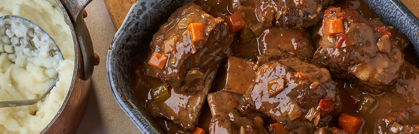 An image of prepared Braised Beef Short Ribs made with short ribs, Swanson® Beef Broth, carrots and red wine.