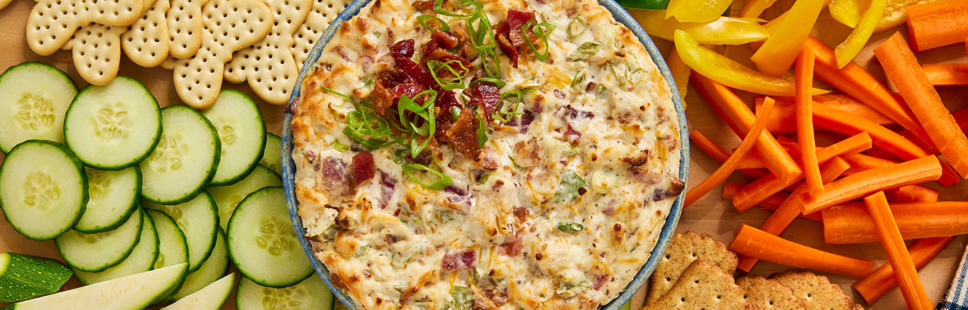 An image of prepared Chicken Bacon Ranch Dip made with bacon, Swanson® Premium White Chunk Chicken, cream cheese, sour cream, ranch, green onions and Cheddar Jack cheese.