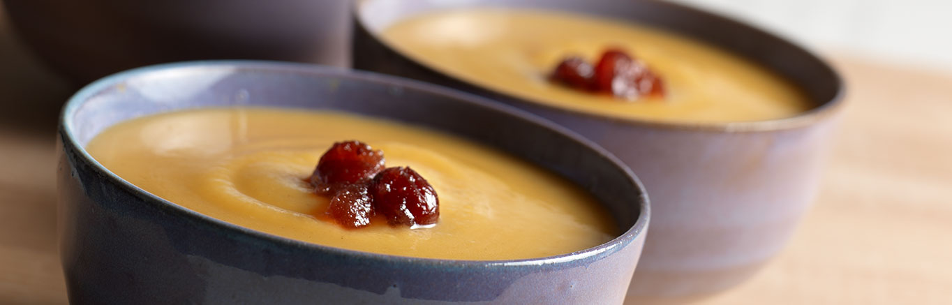An image of prepared Cream of Pumpkin Soup with Cranberry Drizzle made with Swanson® Vegetable Broth, cranberry sauce and calabaza squash.