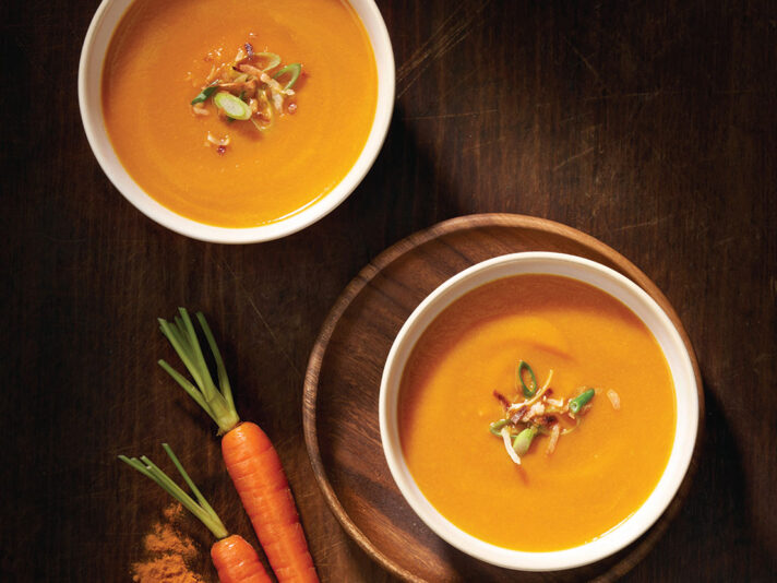 An image of prepared Creamy Carrot Ginger Soup made with onion, ginger root, turmeric, carrots, Swanson® Chicken Bone Broth, coconut milk, coconut and green onions.