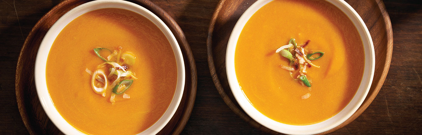 An image of prepared Creamy Carrot Ginger Soup made with onion, ginger root, turmeric, carrots, Swanson® Chicken Bone Broth, coconut milk, coconut and green onions.