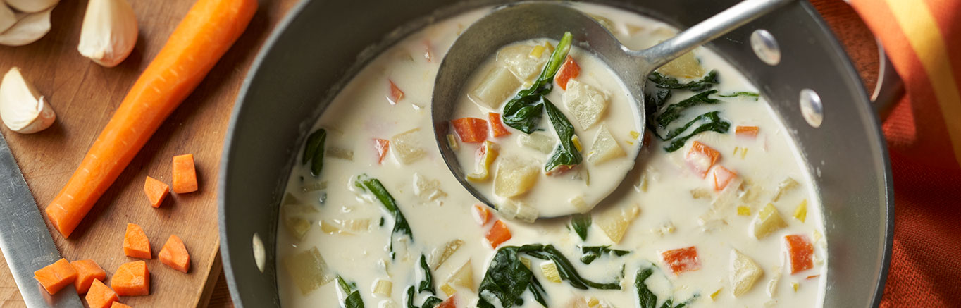 An image of prepared Garlicky Potato Leek Soup made with Yukon Gold potatoes, leeks, carrots, garlic, Swanson® Chicken Broth, light cream and baby spinach.