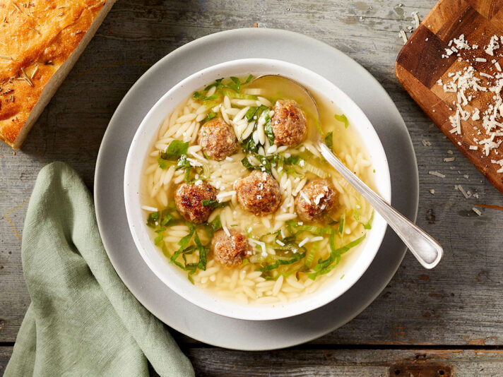 An image of prepared Italian Wedding Soup made with ground beef, Parmesan cheese, Swanson® Chicken Broth, orzo pasta and escarole.