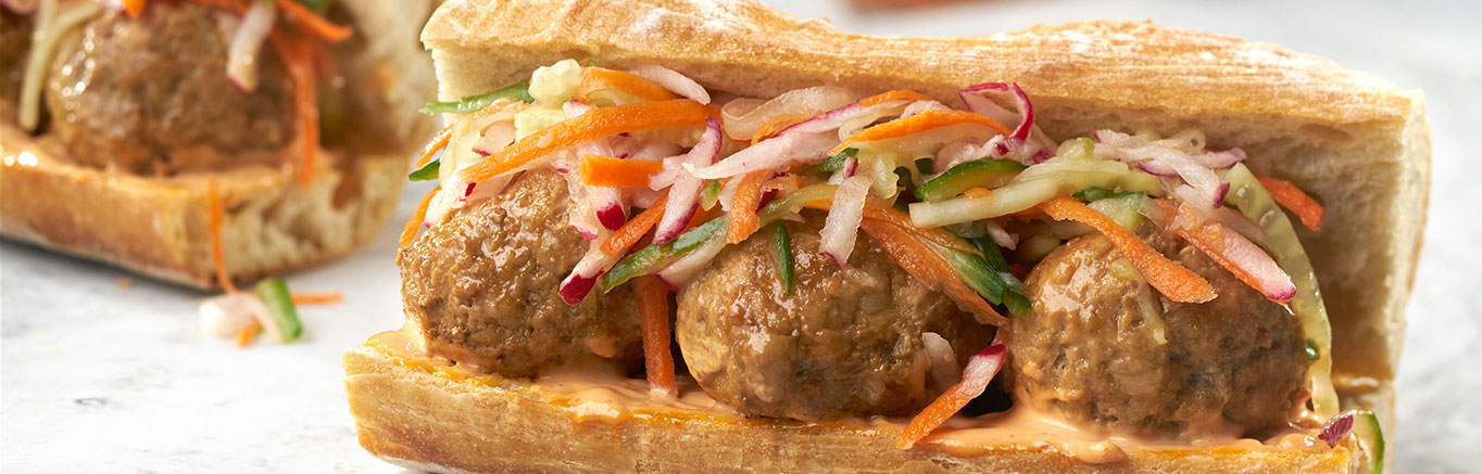 An image of prepared Pork Meatball Banh Mi Sandwiches made with ground pork, Swanson® Beef Broth, sriracha hot chili sauce, mayonnaise, carrot, radish, cucumber and hard rolls.