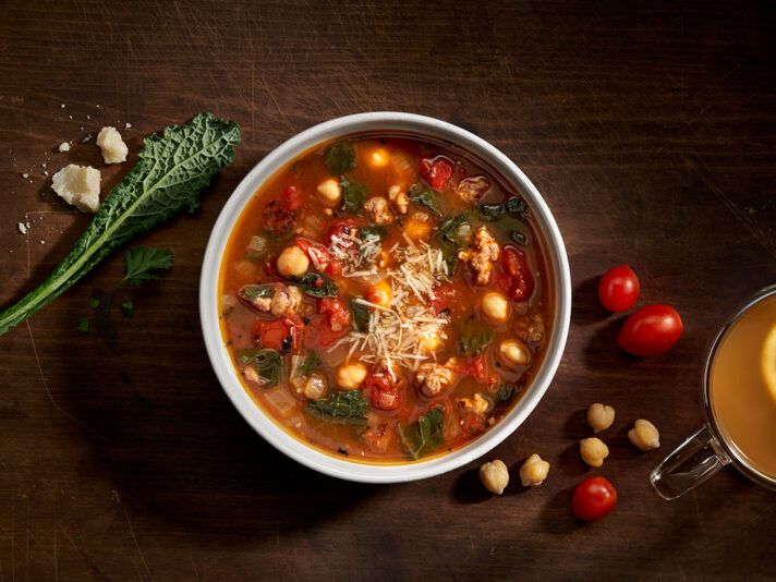 An image of prepared Sausage Kale Soup made with pork sausage, onion, fired roasted tomatoes, kale, chickpeas, Swanson® Chicken Bone Broth, Parmesan cheese and parsley.