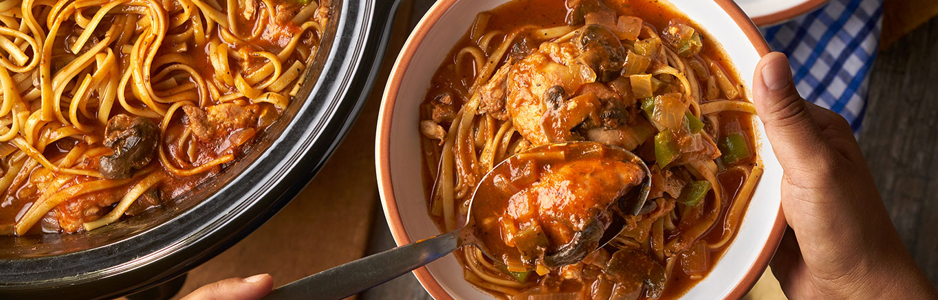 An image of prepared Savory Slow-Cooked Chicken Cacciatore made with mushrooms, onions, green bell pepper, garlic, chicken thighs, red wine, Swanson® Chicken Broth or Stock, Prego® Traditional Sauce and linguine.