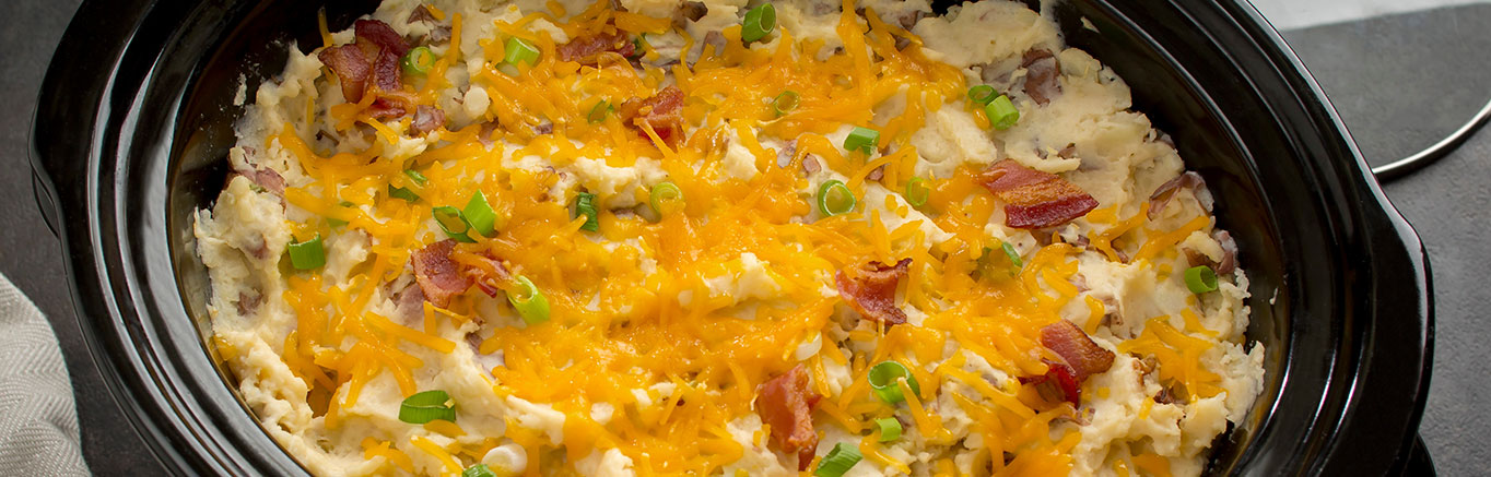 An image of prepared Slow Cooker Loaded Mashed Potatoes made with red potatoes, Swanson® Chicken Broth, butter, Cheddar cheese, cream cheese, bacon and green onions.