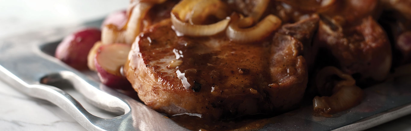 An image of prepared Smothered Pork Chops made with Swanson® Beef Broth, pork chops, onion and garlic.
