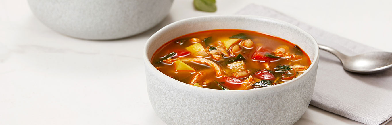 An image of prepared Spanish-Style Chicken & Chickpea Soup made with onion, red bell pepper, yellow squash, chicken, chickpeas, Swanson® Chicken Bone Broth and baby spinach.