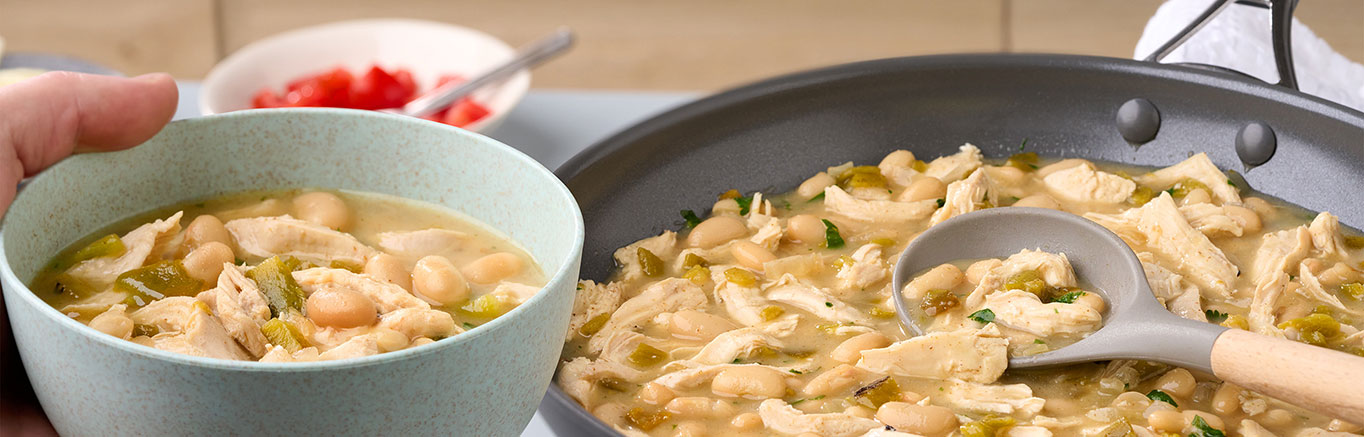 An image of prepared Spicy Verde Chicken & Bean Chili made with Swanson® Chicken Broth, chicken, white navy beans, green chiles, flour tortillas, Monterey Jack cheese and cilantro.