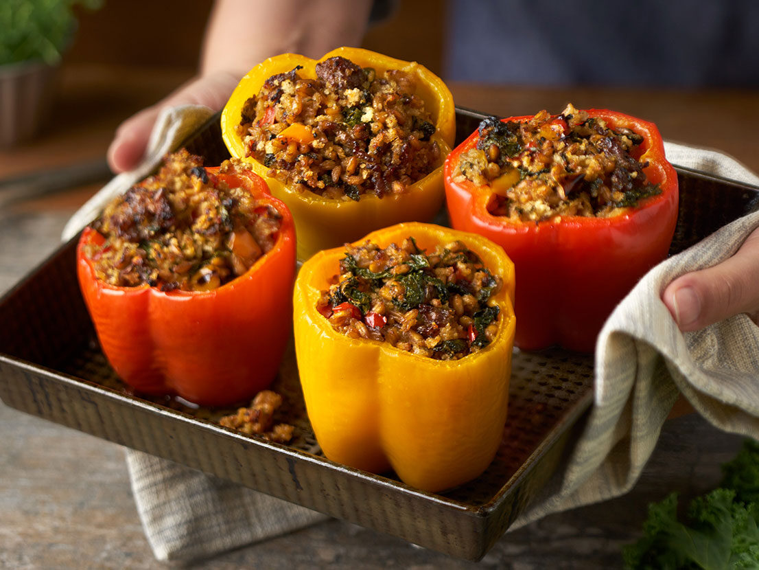 An image of prepared Stuffed Peppers with Kale & Farro made with onion, sweet Italian pork sausage, Swanson® Chicken Broth, farro, kale, panko and Parmesan cheese.