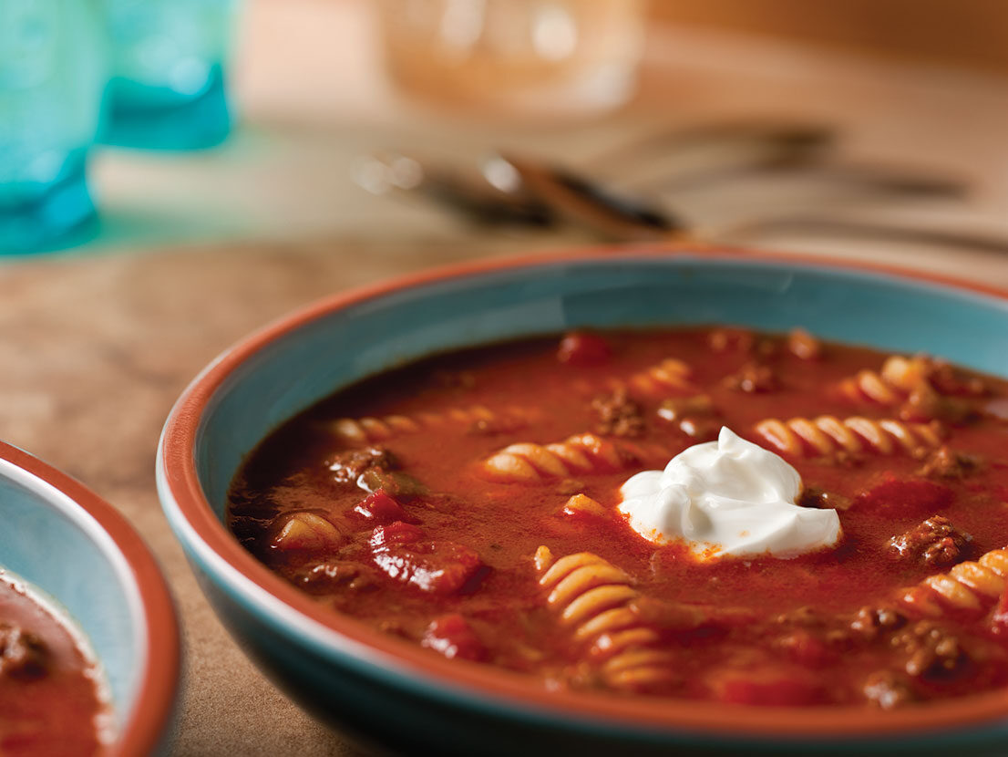 An image of prepared Taco Twist Soup made with ground beef, chili powder, Swanson® Beef Broth, Pace® Picante Sauce, canned diced tomatoes, rotini pasta and sour cream.